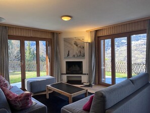 Un salon chaleureux avec une cheminée, de grandes fenêtres et une vue sur l’extérieur.