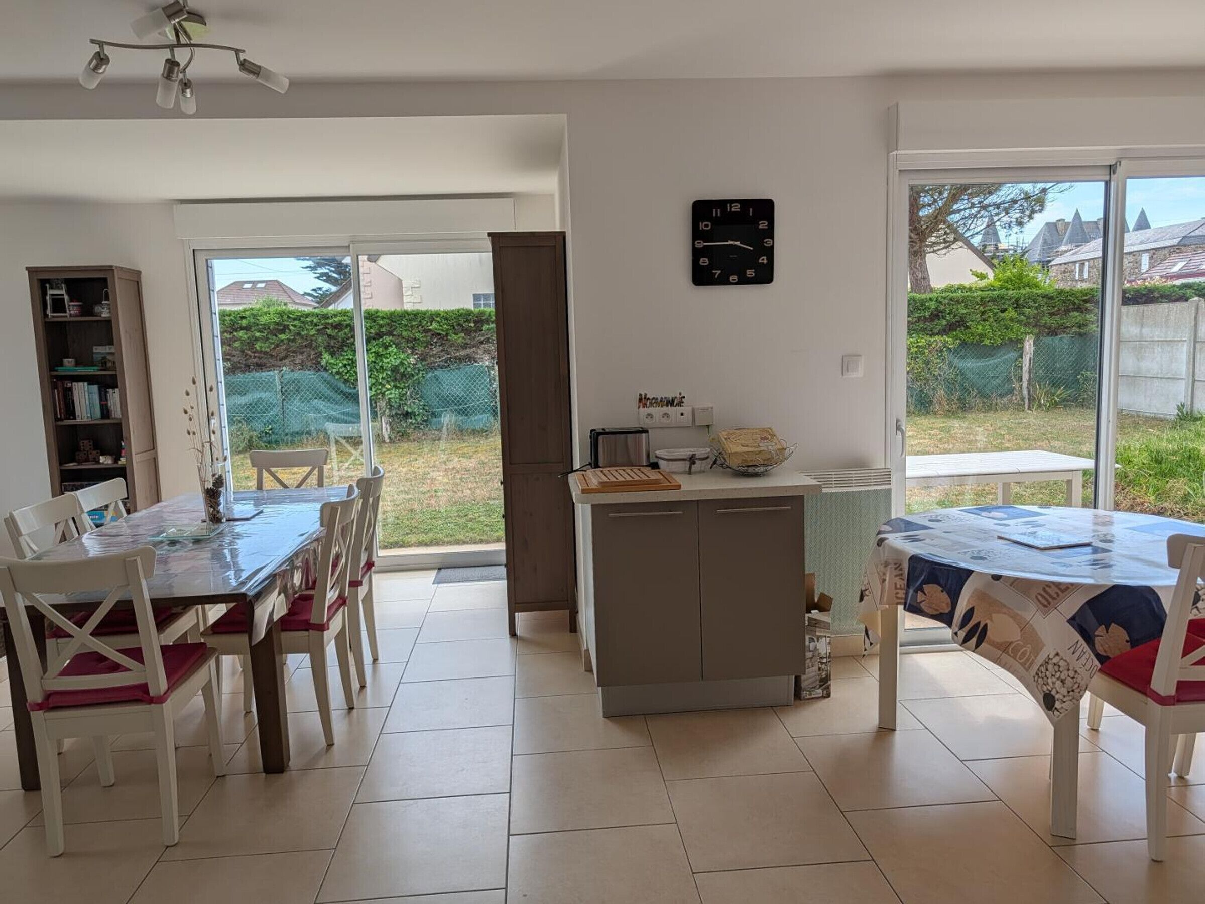Un espace repas avec une table et des chaises, un comptoir de cuisine, une horloge et une vue sur l’extérieur.
