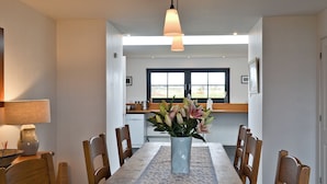 A dining area with a table, chairs, a vase of flowers, pendant lights, and a view of the kitchen and outdoors through a window. - 3 bedroom accommodation in Roag, Isle of Skye (Roag, Isle of Skye)