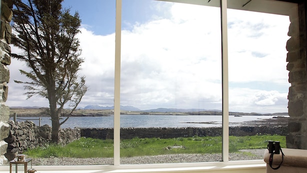 A room with a large window overlooking a body of water, a stone wall, and a tree. - 3 bedroom accommodation in Roag, Isle of Skye (Roag, Isle of Skye)