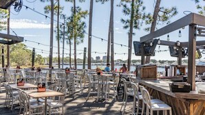 Un espace de restauration en plein air, avec des tables et des chaises, donnant sur une étendue d’eau où se trouvent des bateaux.