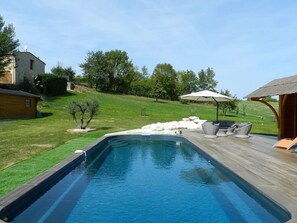 A swimming pool with a wooden deck, outdoor furniture, and a thatched-roof structure.