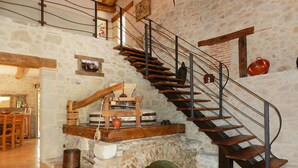 Un interior rústico con chimenea de piedra, escalera de madera y zona de comedor.