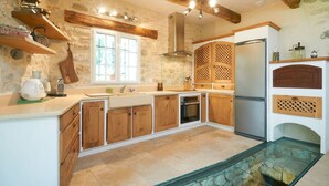 Una cocina con armarios de madera, encimera de piedra, horno empotrado y pileta con fondo de vidrio.