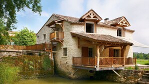 Una casa de piedra con balcón de madera y un pequeño puente de madera sobre un estanque.