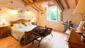 Un dormitorio acogedor con una cama de madera, una silla, un escritorio con una máquina de coser y una ventana con vistas a zonas verdes.