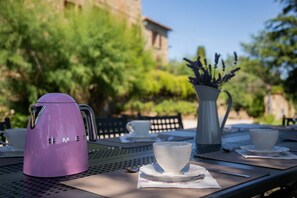 A table set outdoors with a purple electric kettle, white cups, saucers, and a vase with lavender.