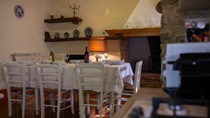 Ein Essbereich mit einem langen Tisch, gedeckt für sechs Personen, umgeben von weißen Stühlen. Eine Holzablage darüber beherbergt mehrere dekorative Teller und einen Kerzenleuchter. Eine Tischlampe sorgt für warmes Licht.