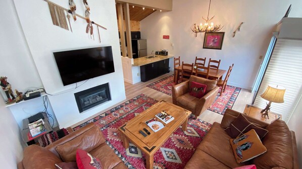 Ein modernes Wohnzimmer mit Flachbildfernseher, Kamin, Essbereich mit Holzkohle und einer Küche im Hintergrund.