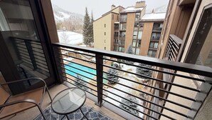 Ein Balkon mit Glastür, einem kleinen runden Tisch und Blick auf ein Schwimmbad sowie Gebäude im Hintergrund.