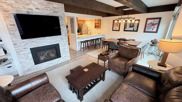 Ein modernes Wohnzimmer mit Kamin, Ledersofas, einer Essecke mit Bar und einer Küche im Hintergrund.