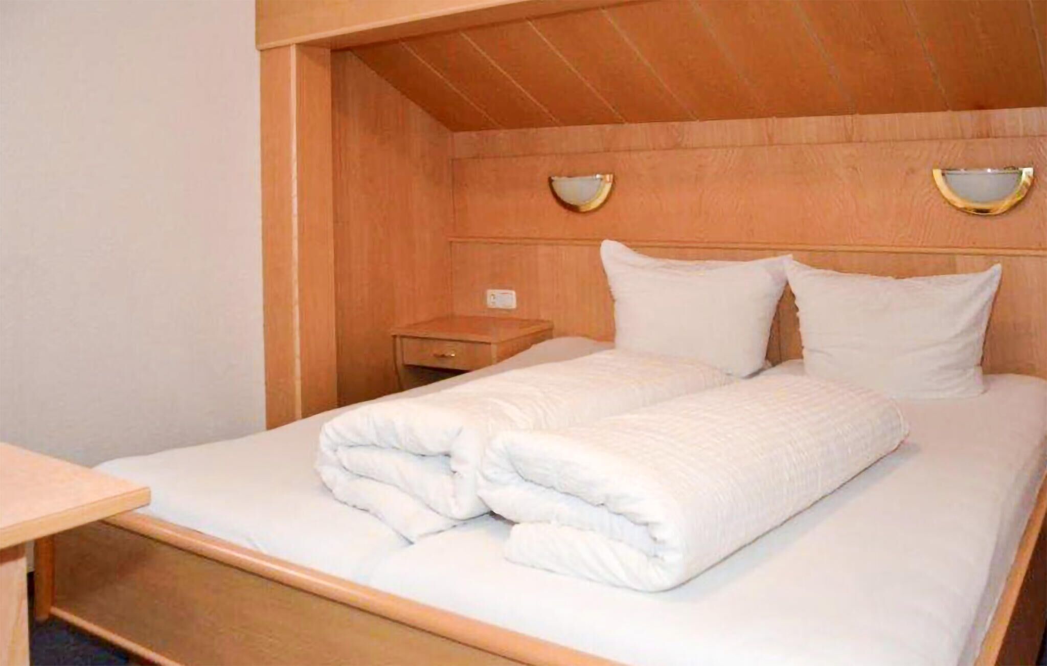 Un lit bien fait, avec du linge de lit blanc et des oreillers, une tête de lit en bois et deux tables de chevet avec des lampes.