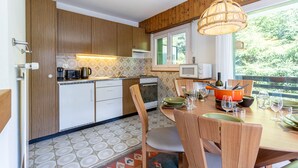 Une cuisine moderne avec des meubles en bois, une table à manger pour quatre personnes et une grande fenêtre donnant sur un paysage verdoyant.