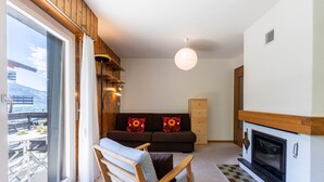 Un salon comprenant un canapé, une chaise en bois, une cheminée et une grande fenêtre donnant sur un balcon.