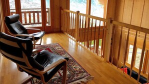Une cabane en bois avec un balcon, deux fauteuils en cuir et un tapis à motifs.