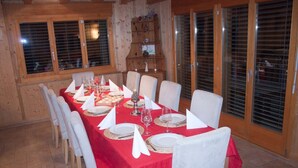 Un coin repas avec une nappe rouge, des chaises blanches et un buffet en bois en arrière-plan.