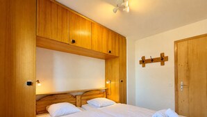 Cama doble con ropa blanca, cabecera de madera y armario de madera con espejo.