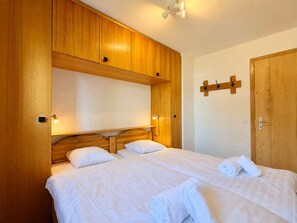 A double bed with white linens, wooden headboard, and a wooden wardrobe with a mirror. - Gentianes G 010 - COSY apartment 8 pers (Veysonnaz)