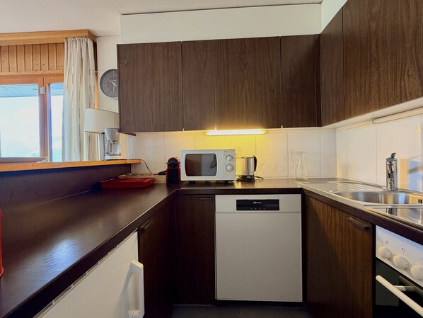 A compact kitchen with dark wooden cabinets, a white dishwasher, a microwave, and a coffee maker.