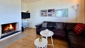A living room with a fireplace, a sofa, a TV, and a small table with a cup. - Gentianes G 010 - COSY apartment 8 pers (Veysonnaz)