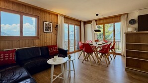 Una habitación con interior de madera, un sofá de cuero negro, una mesa de comedor con sillas rojas y ventanas amplias.