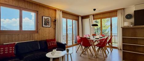 Ein Zimmer mit Holzvertäfelung, einem schwarzen Ledersofa, einem Esstisch mit roten Stühlen und großen Fenstern.