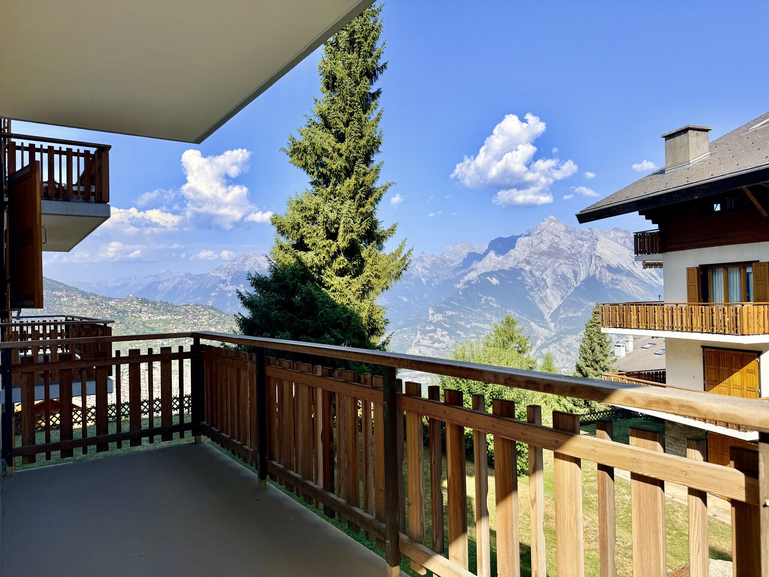 A balcony with a wooden railing overlooking a mountain landscape.