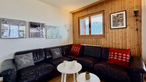 Una sala de estar acogedora con un sofá de cuero negro, una mesa de centro blanca y una pared revestida de madera con cuadros enmarcados.