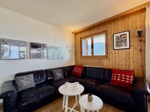 A cozy living room with a black leather sofa, white coffee table, and a wooden paneled wall with framed pictures. - Gentianes G 010 - COSY apartment 8 pers (Veysonnaz)