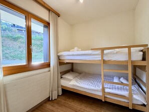 A bunk bed room with a window, wooden floor, and a view of greenery outside.