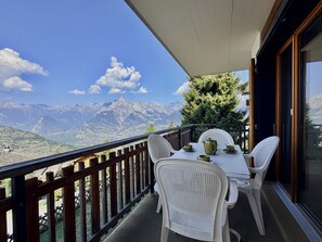 A balcony with a table and chairs, overlooking a mountainous landscape.