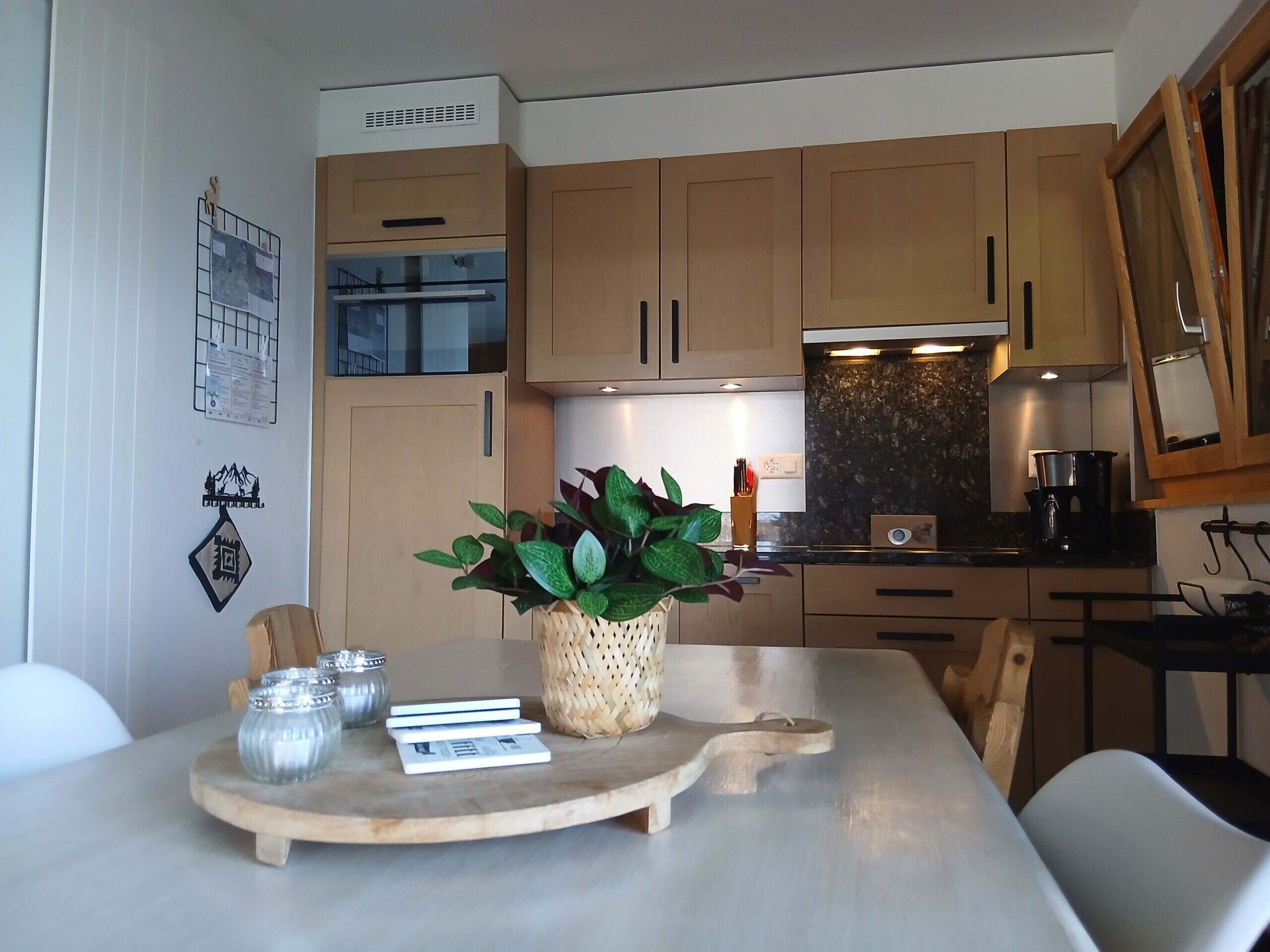 Cozinha moderna com armários de madeira, uma mesa de jantar com um jogo americano e um vaso com planta.