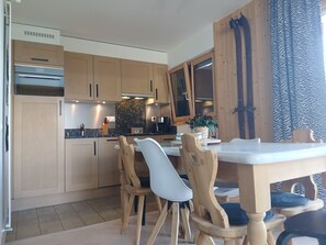 Una cocina moderna con armarios de madera, horno empotrado y un comedor con mesa blanca y sillas de madera.