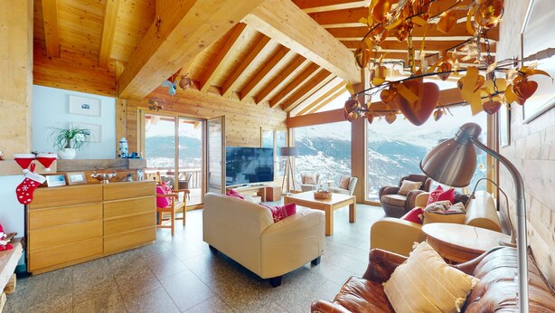 A cozy living room with a wooden ceiling, a large TV, and a view of snowy mountains.