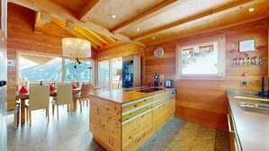 A wooden cabin interior with a kitchen, dining area, and large windows offering mountain views.