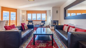 A modern living room with leather sofas, a glass coffee table, and a fireplace. Large windows offer a view of snow-capped mountains. - Myosotis 10 - QUIET apartment 8 pers (Veysonnaz)
