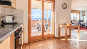 A kitchen with a built-in oven, a dining area with a table and chairs, and a sliding glass door leading to a balcony with a mountain view. - Myosotis 10 - QUIET apartment 8 pers (Veysonnaz)