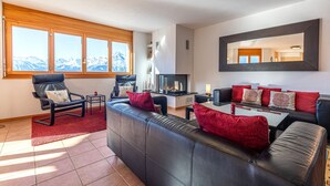 A modern living room with a fireplace, leather sofas, and a large window with a mountain view. - Myosotis 10 - QUIET apartment 8 pers (Veysonnaz)