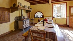 A rustic kitchen with wooden beams, a long dining table set for four, and a window with a view. - Spacious and cozy family gîte, pets allowed, up to 10 people (Saint-Martin-la-Sauveté)