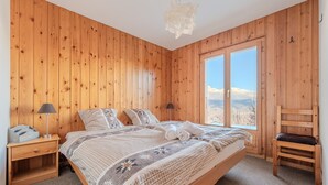 A wooden-paneled bedroom with a large bed, two bedside tables, a chair, and a view of the mountains through a window. - Fontannets 008 QUIET & SUPERIOR chalet 10 pers (Salins)