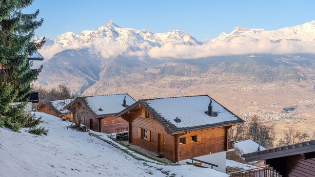 A wooden cabin with a snow-covered roof, set against a backdrop of snow-capped mountains and a clear sky. - Fontannets 008 QUIET & SUPERIOR chalet 10 pers (Salins)