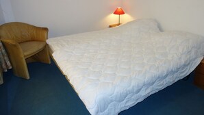 A bedroom with a bed, a chair, a nightstand, and a lamp.