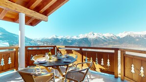 Une terrasse en bois avec une table et des chaises, d’où l’on peut admirer des montagnes enneigées.