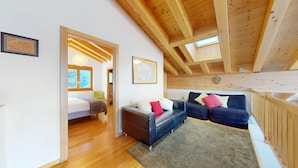 Un loft spacieux avec de hauts plafonds, des poutres apparentes, un coin salon confortable avec un canapé et des fauteuils, un lit et une petite table.