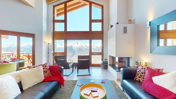 Un salon spacieux avec une cheminée, de grandes fenêtres offrant une vue sur les montagnes et un coin salon confortable.