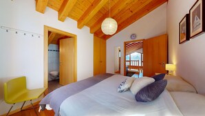 Une chambre à coucher comprenant un lit, une chaise, un plafond en bois, un luminaire suspendu et une porte donnant sur une salle de bain.