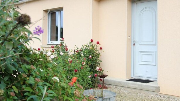 A house with a beige exterior, a white door, and a window. There is a garden with various plants and flowers in front of the house. - Independent house for 6 in Barneville-Carteret with WiFi and bikes (Barneville-Carteret)