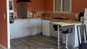 A compact kitchen with a built-in oven, a black range hood, a window with blinds, a sink, and a bar stool. - Independent house for 6 in Barneville-Carteret with WiFi and bikes (Barneville-Carteret)