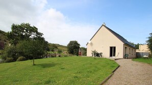 A single-story building with a sloped roof, a gravel driveway, and a grassy lawn with scattered yellow flowers. - Independent house for 6 in Barneville-Carteret with WiFi and bikes (Barneville-Carteret)