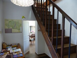 A wooden staircase leading to a second floor, a dining area with chairs, a table with books, and a map on the wall.